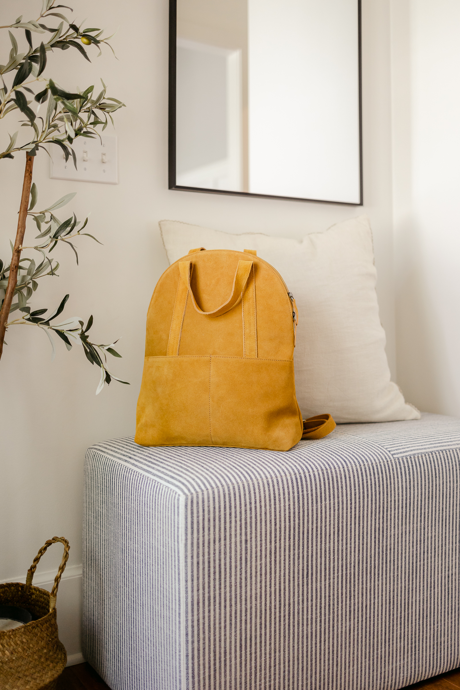 sunny yellow suede backpack sitting on a striped bench in the entryway of the home