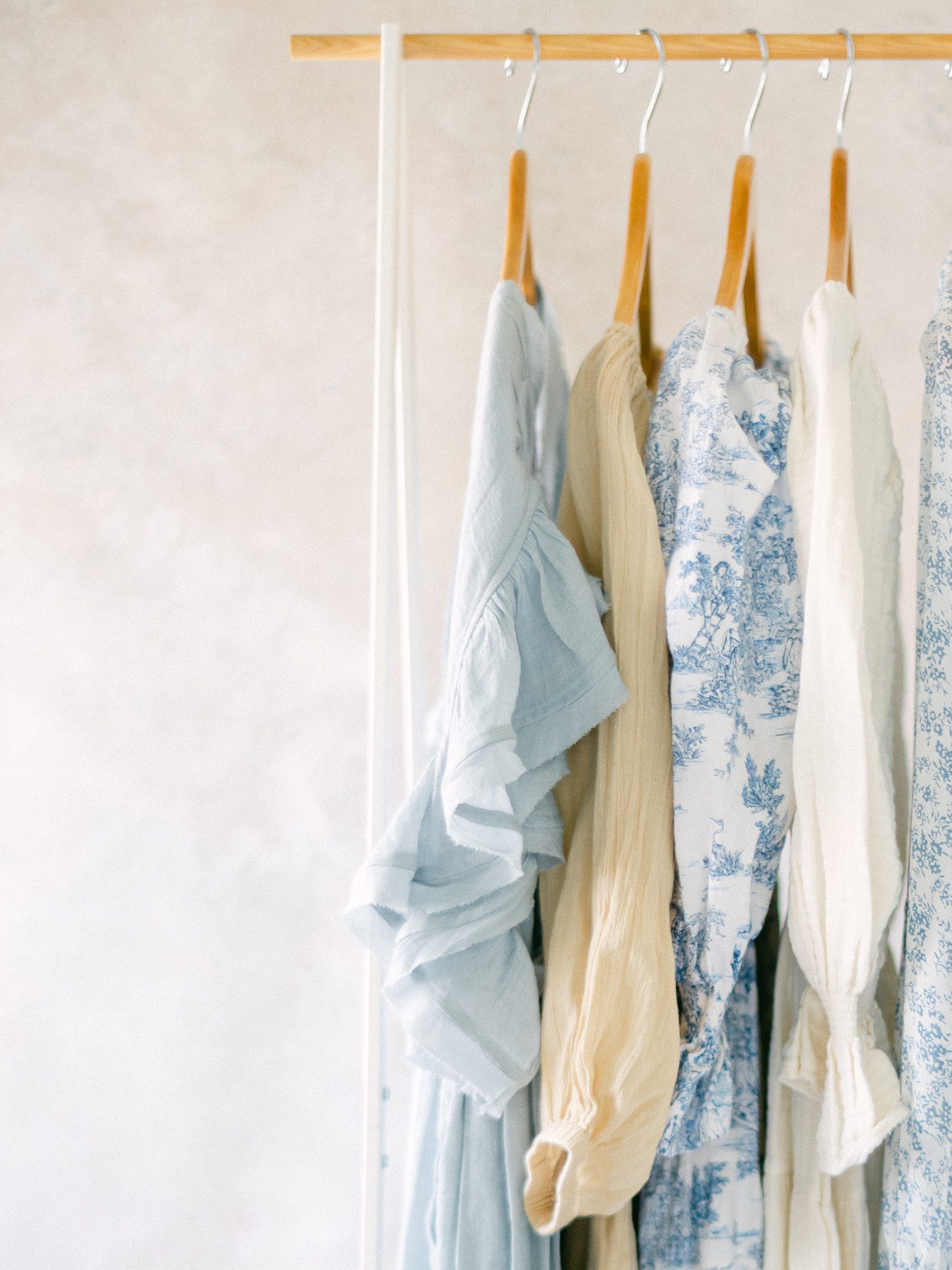 clothing rack with cream, white, and light blue floral dresses hanging in front of a neutral backdrop